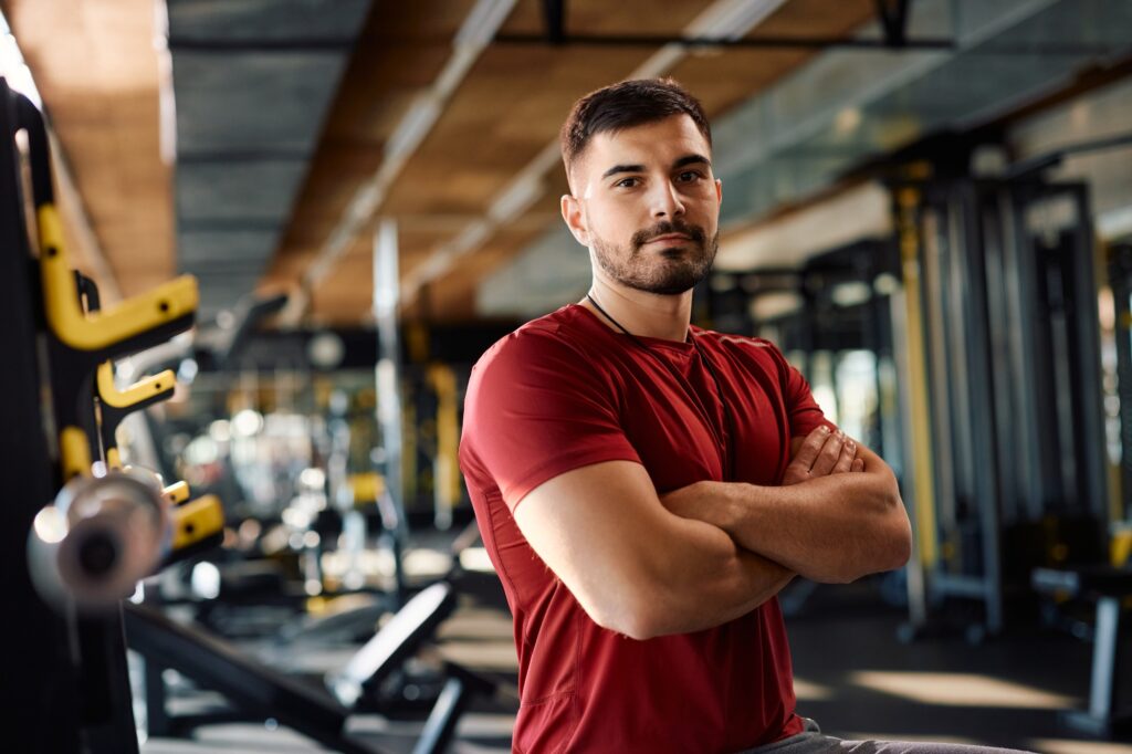 Confident personal trainer with arms crossed in a gym looking at camera.
