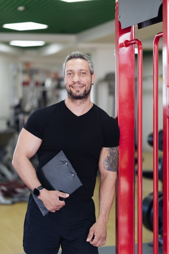 Daily sport routine, healthy lifestyle. Gray haired smiling coach man portrait in the gym